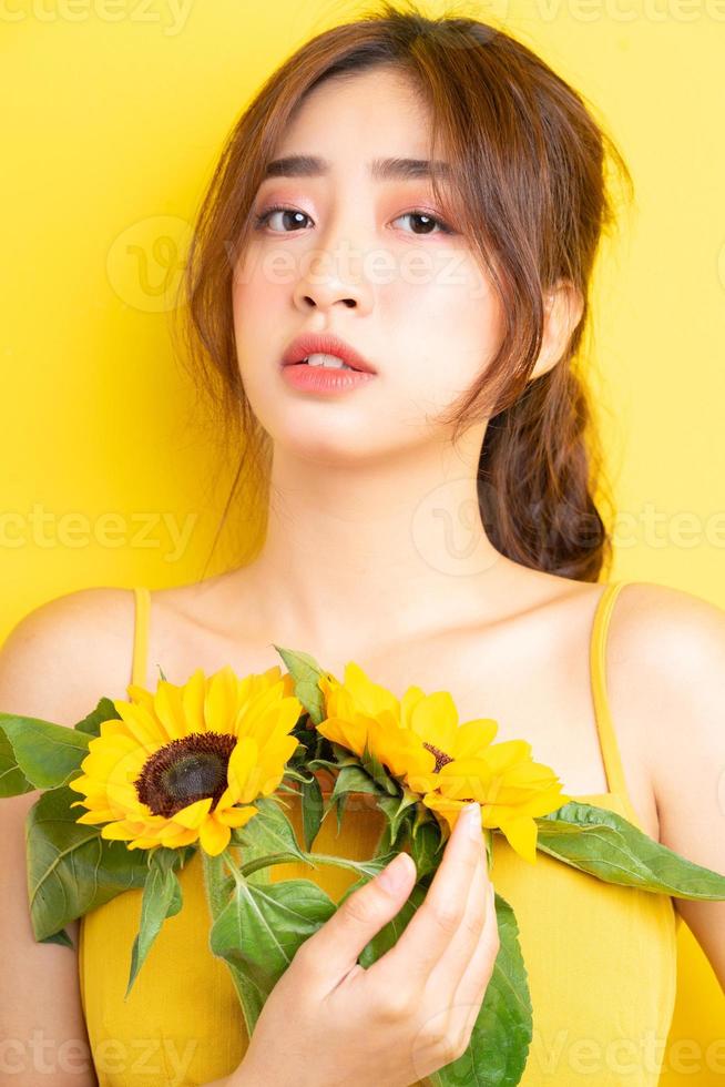 belle femme asiatique tenant et posant avec tournesol sur fond jaune photo