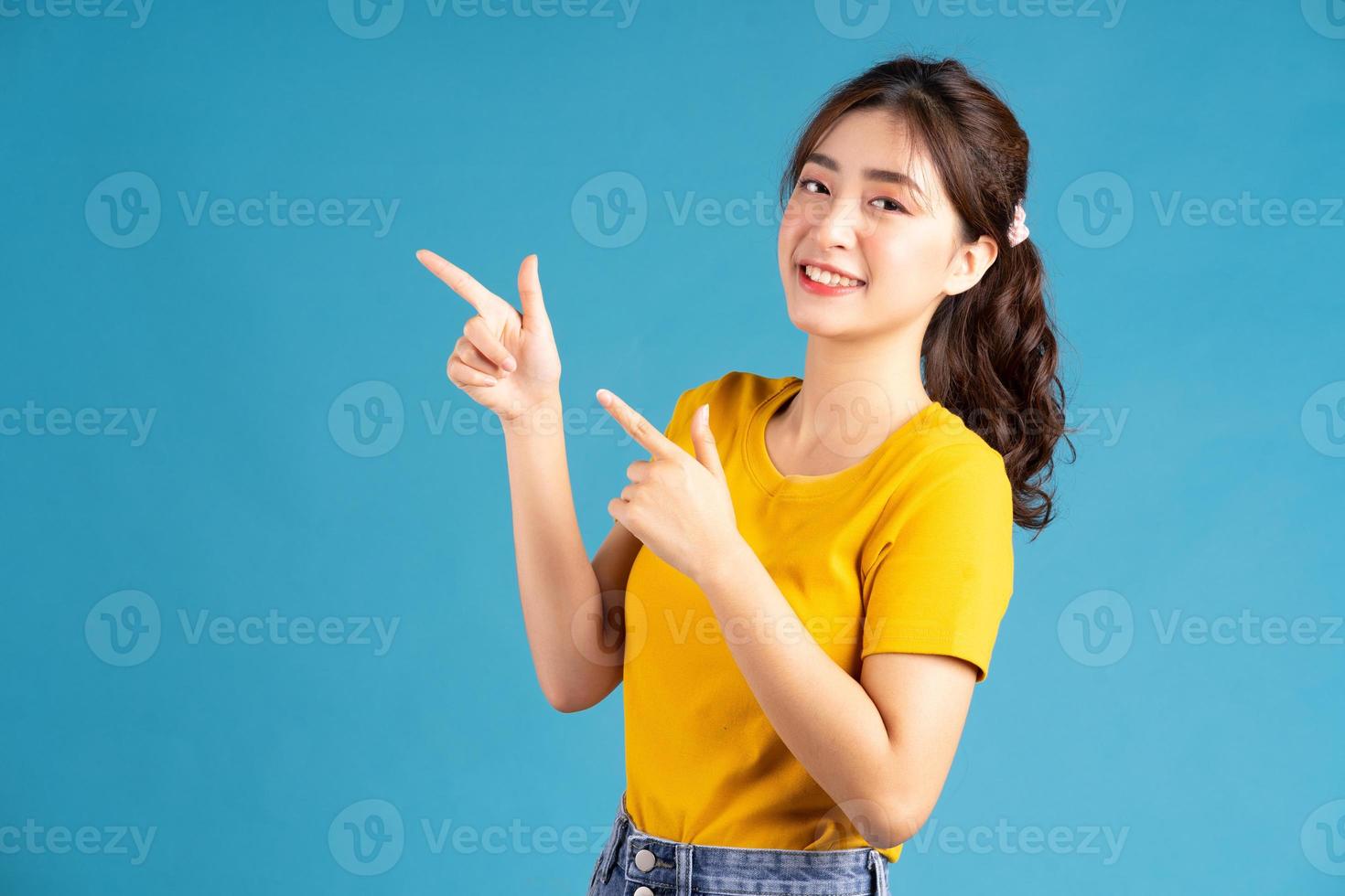 jeune femme asiatique à l'aide du doigt pour pointer sur baclground bleu photo