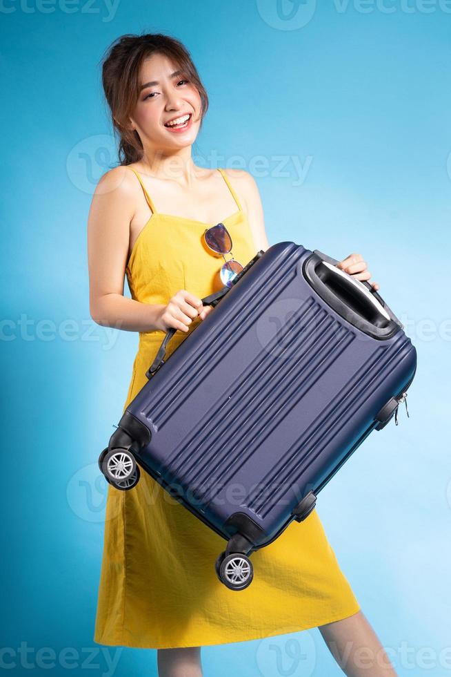 Jeune femme asiatique tenant une valise sur fond bleu, concept d'été photo