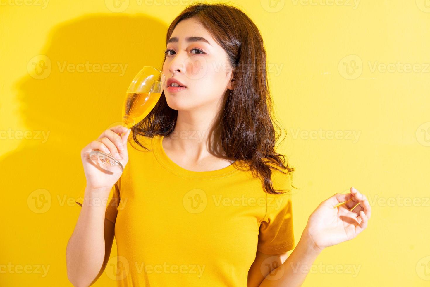 jeune femme asiatique buvant du vin et posant sur fond jaune photo