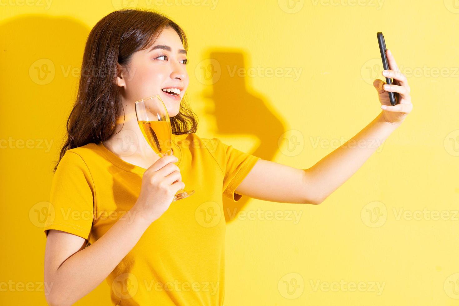 jeune femme asiatique buvant du vin et posant sur fond jaune photo