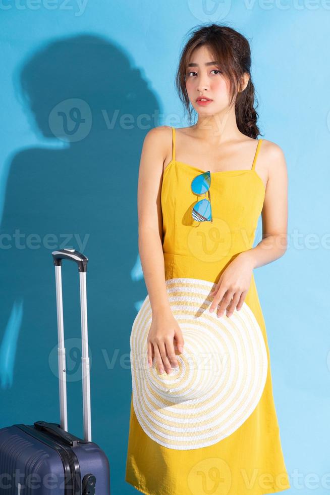 Jeune femme asiatique tenant une valise sur fond bleu, concept d'été photo