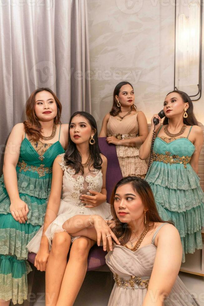 une groupe de asiatique femmes dans glamour et luxueux vêtements sont séance sur le canapé avec leur copains après faire la fête photo