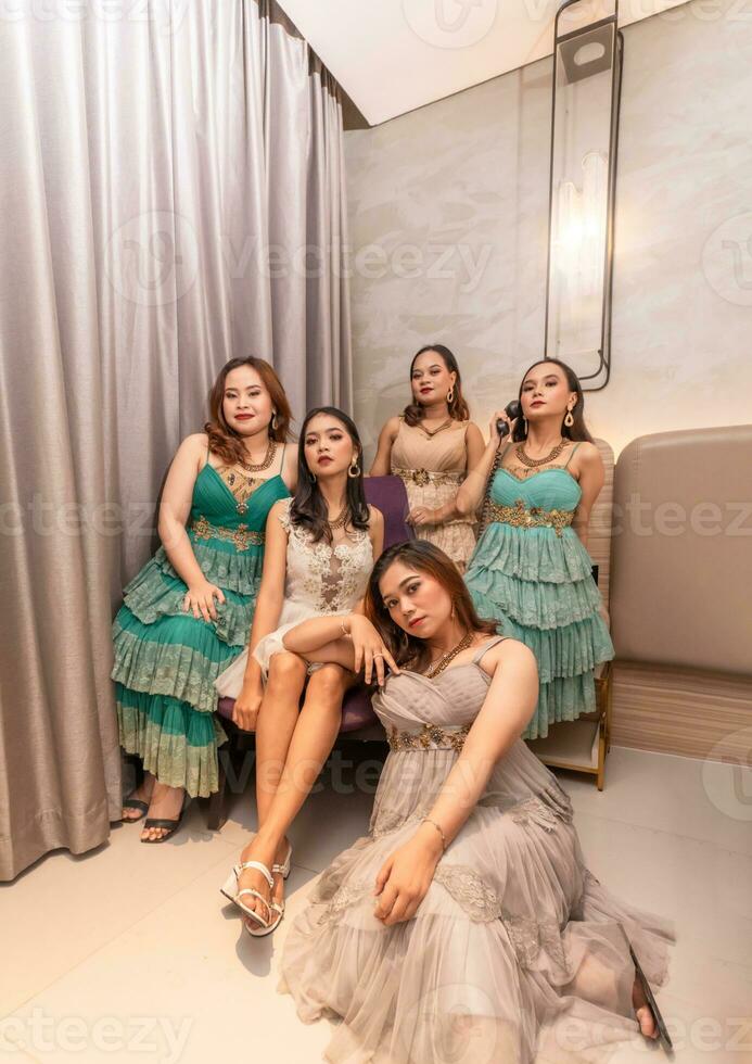 une groupe de asiatique femmes dans glamour et luxueux vêtements sont séance sur le canapé avec leur copains après faire la fête photo