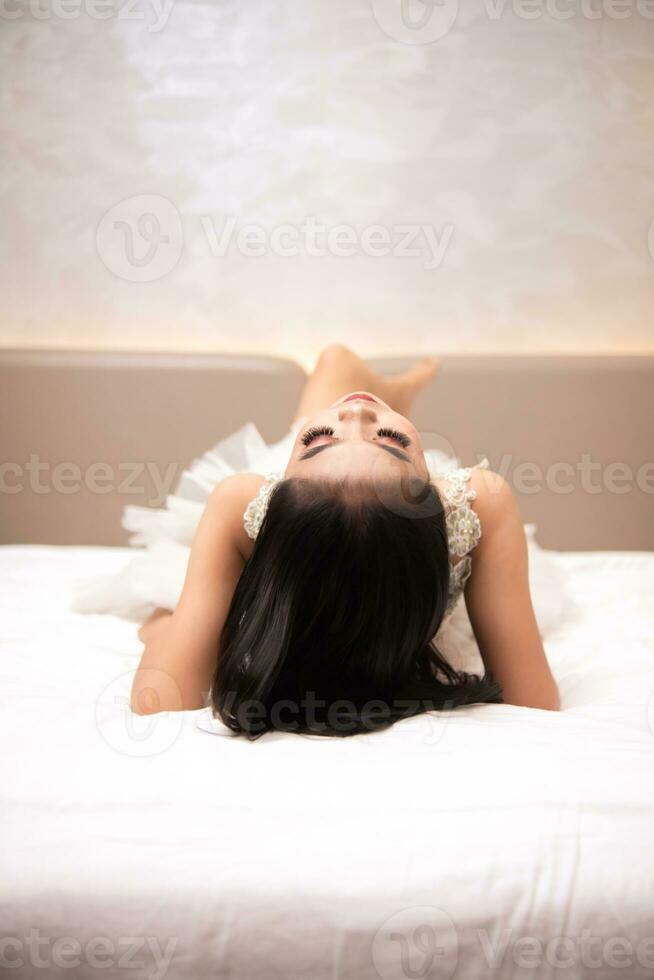 un asiatique femme avec noir cheveux est en train de dormir sur une blanc lit dans un élégant Hôtel photo