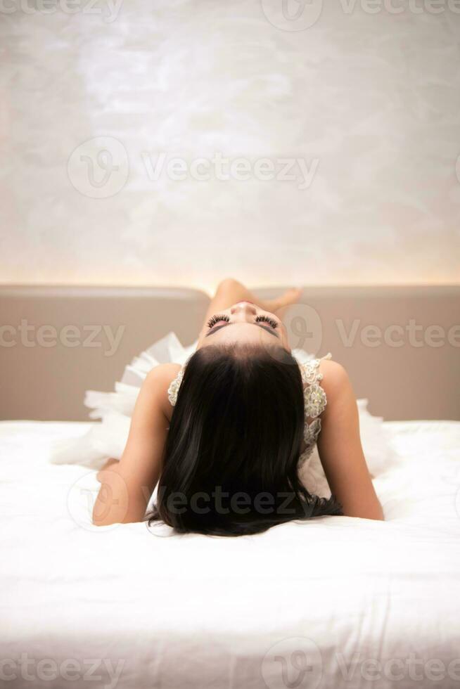 un asiatique femme avec noir cheveux est en train de dormir sur une blanc lit dans un élégant Hôtel photo