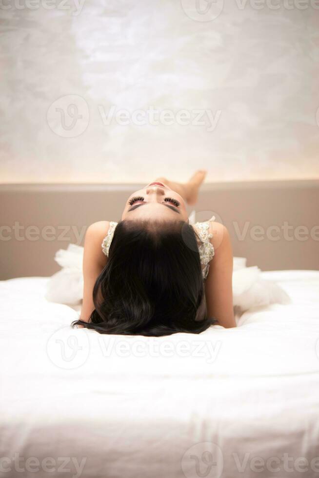 un asiatique femme avec noir cheveux est en train de dormir sur une blanc lit dans un élégant Hôtel photo