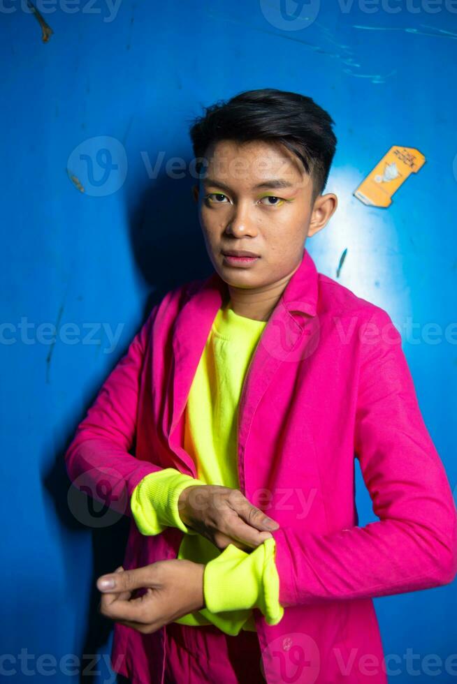 une gay asiatique homme posant très marrant et humoristique tandis que portant une rose costume dans de face de une bleu Contexte photo