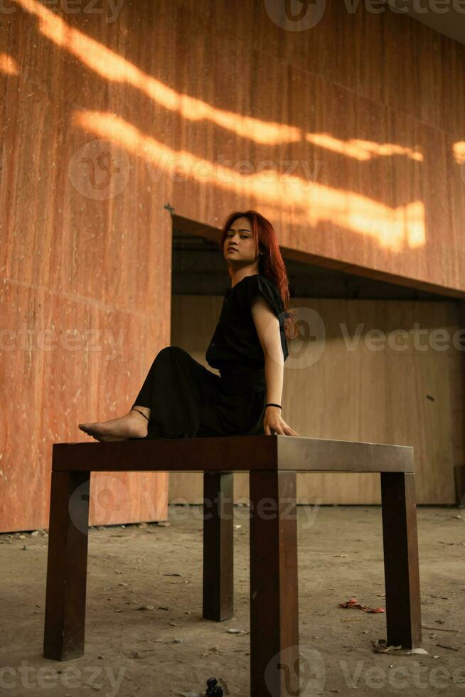 un asiatique homme avec longue cheveux est séance et posant sur une marron table photo