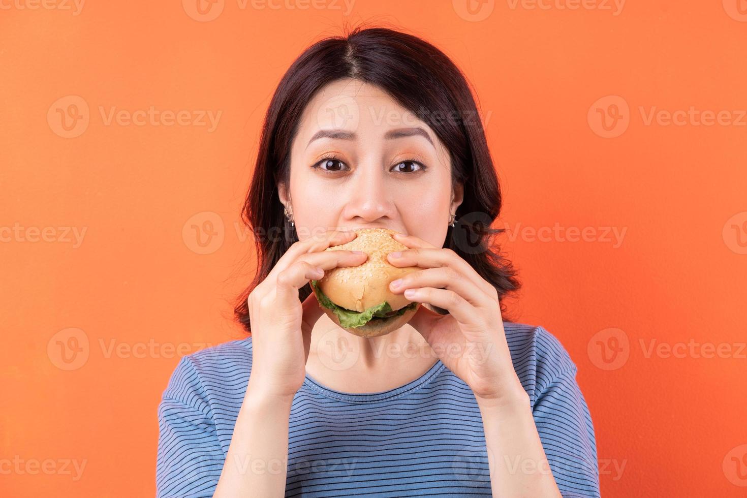 Jeune femme asiatique mangeant un hamburger sur fond orange photo