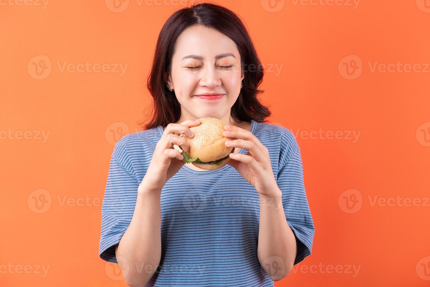 Jeune femme asiatique mangeant un hamburger sur fond orange photo