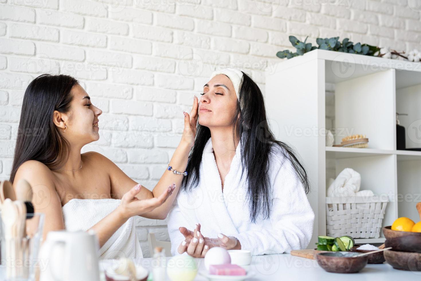 deux belles femmes appliquant une crème pour le visage faisant des procédures de spa photo