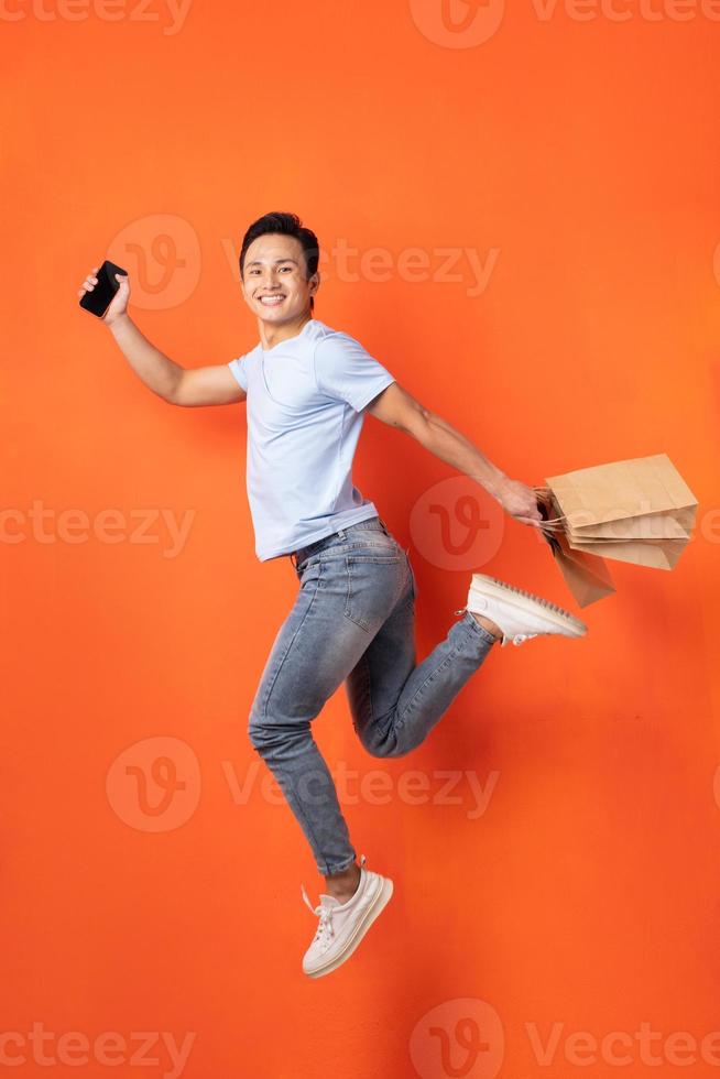 homme asiatique tenant un smartphone et un sac à provisions en sautant photo