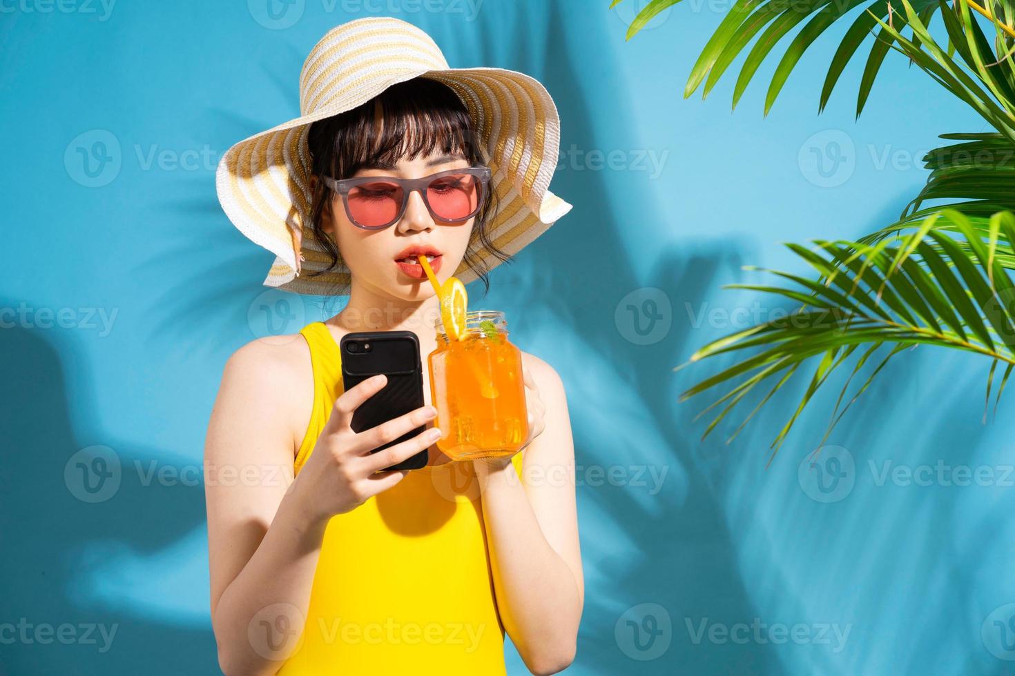 belle femme asiatique portant une combinaison jaune sur fond bleu et buvant du jus, concept d'été photo