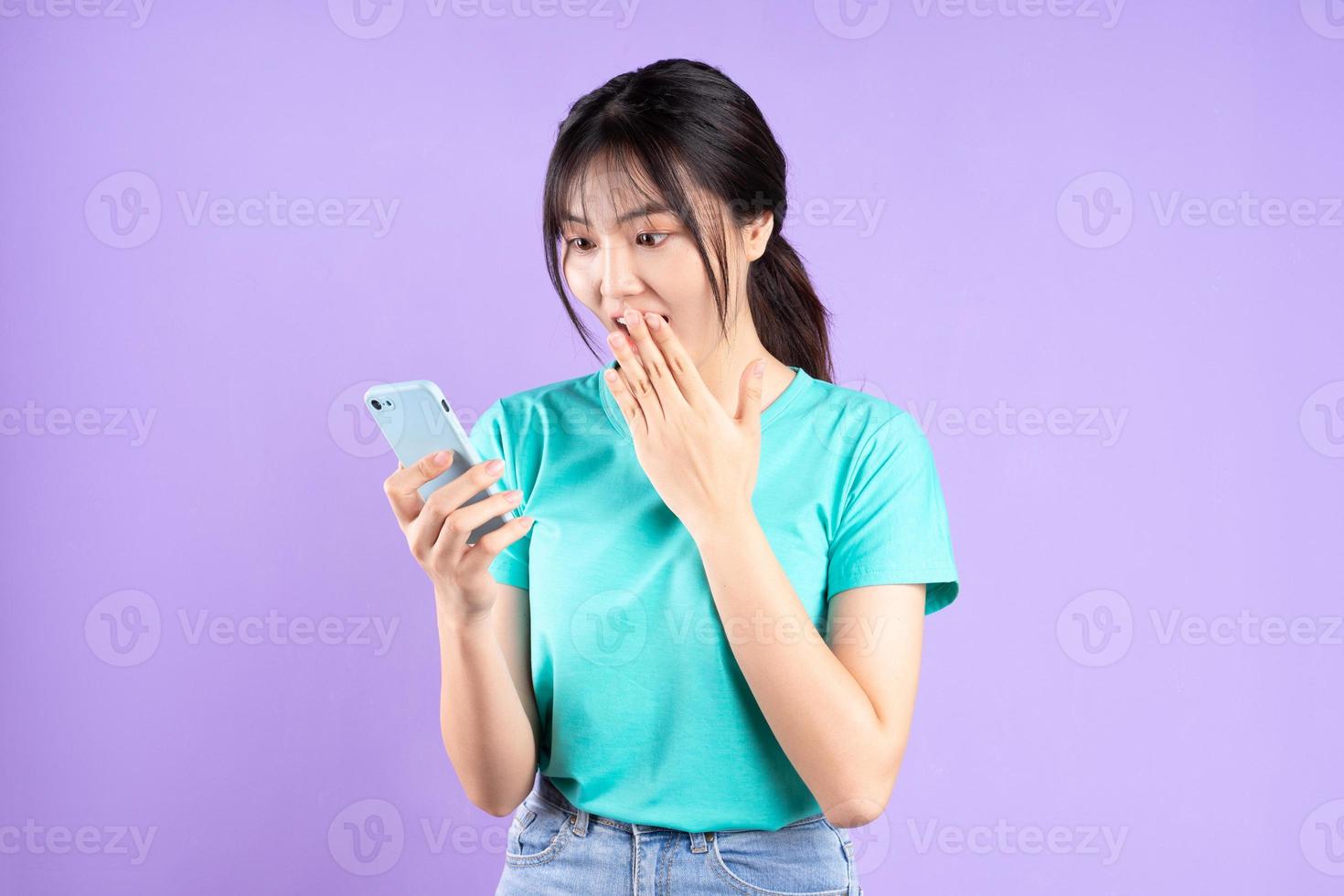 jeune fille asiatique en chemise cyan à l'aide de téléphone sur fond violet photo