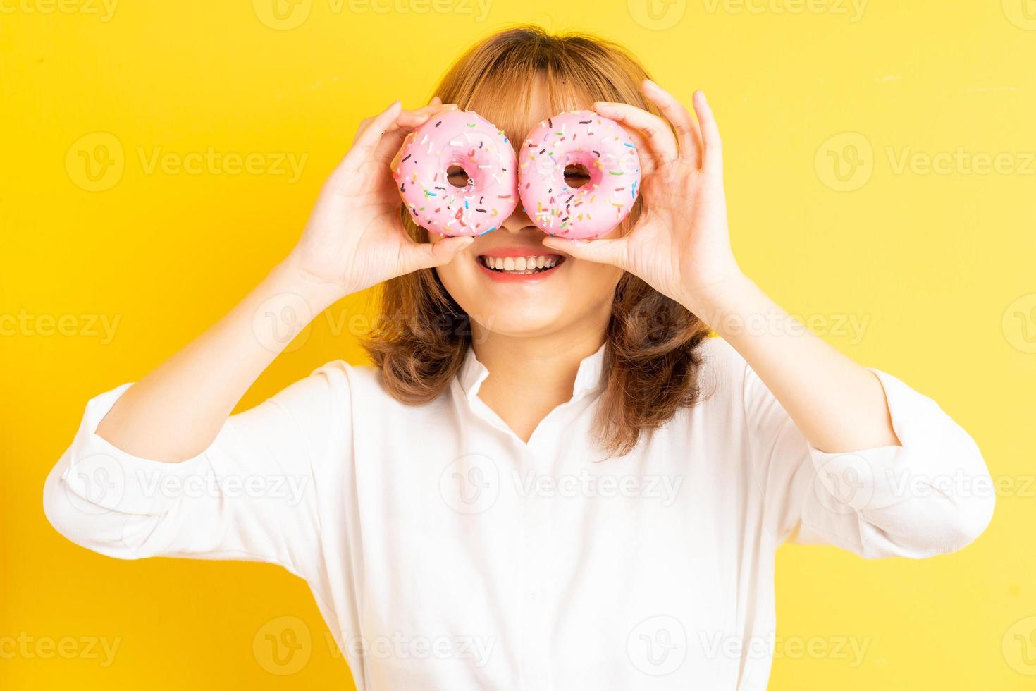 jeune fille asiatique tenant un beignet avec une expression joyeuse sur fond photo