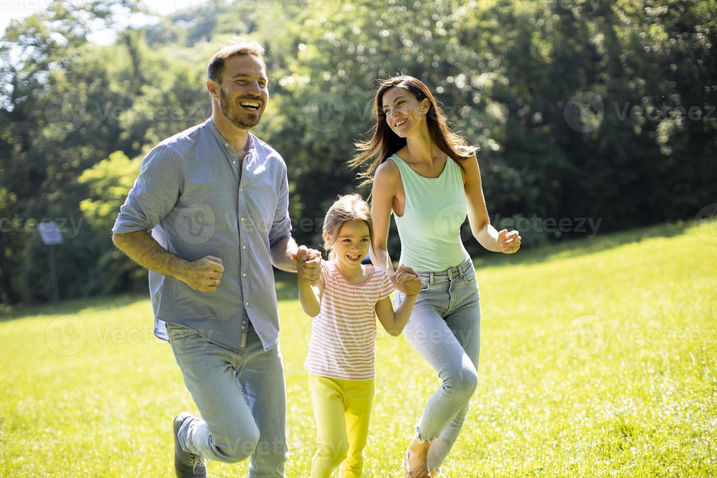 jeune famille heureuse avec une petite fille mignonne qui court dans le parc par une journée ensoleillée photo