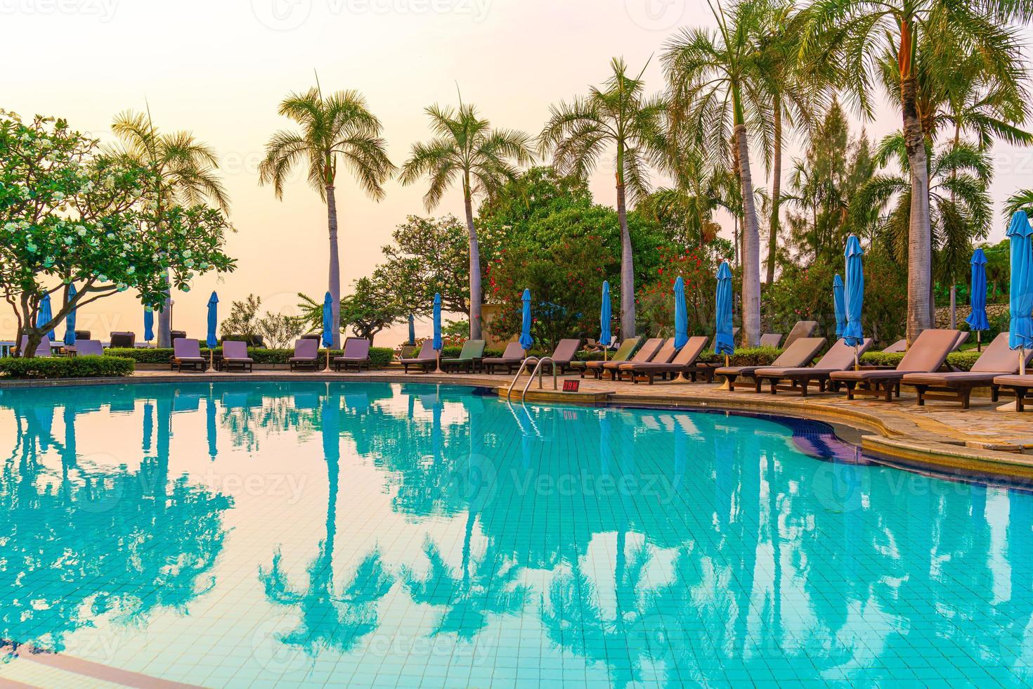 chaises de plage ou lits de piscine avec parasols autour de la piscine au coucher du soleil photo