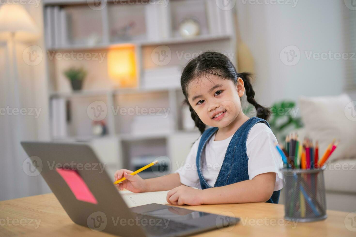 asiatique bébé fille souriant utilisation portable ou l'écriture dessin Couleur sur Remarque livre étude en ligne sur bois table bureau dans vivant pièce à maison. éducation apprentissage en ligne de Accueil concept. photo