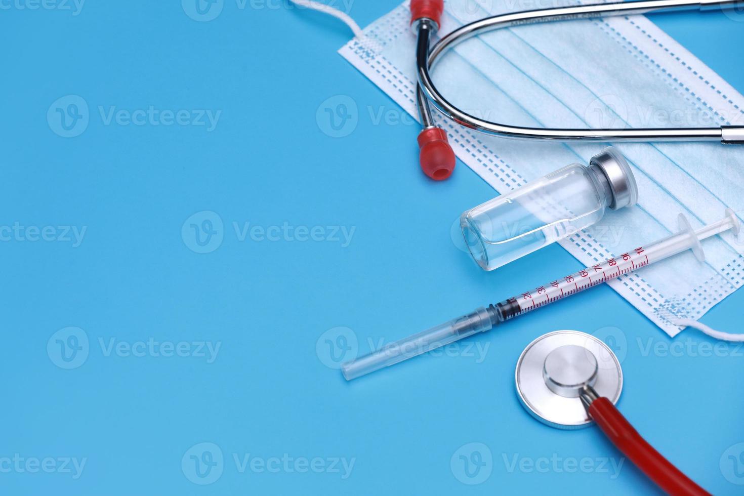 bouteille médicale, flacon, seringue, stéthoscope et masque facial sur fond bleu avec espace de copie. séance de vaccination et amélioration de l'immunité. photo