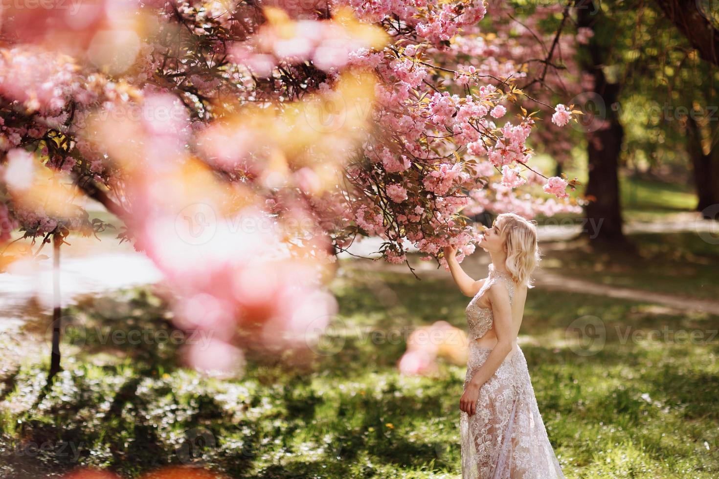 belle fille apprécie le parfum de l'arbre en fleurs. portrait d'une belle femme avec un cerisier en fleurs - une fille respire le parfum des fleurs avec les yeux fermés - concept printemps, nature et beauté photo