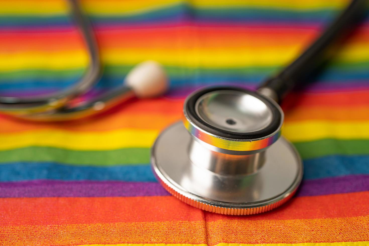 stéthoscope noir sur fond de drapeau arc-en-ciel, symbole du mois de la fierté lgbt célèbre chaque année en juin social, symbole des gays, lesbiennes, bisexuels, transgenres, droits de l'homme et paix. photo