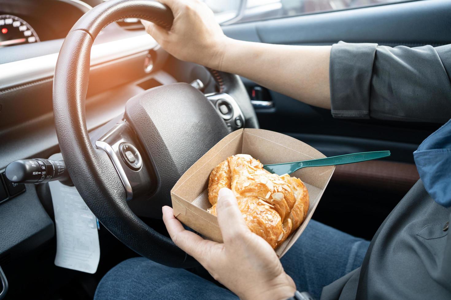 dame asiatique tenant de la nourriture de boulangerie dans une voiture, dangereuse et risquant un accident. photo