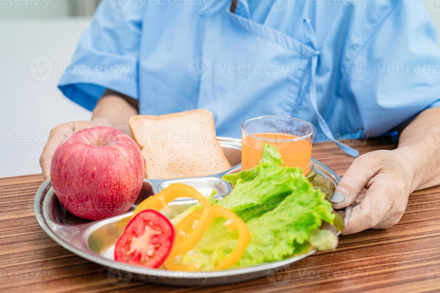 Une patiente asiatique âgée ou âgée de vieille dame mangeant un petit-déjeuner de légumes sains avec espoir et heureuse assise et affamée sur son lit à l'hôpital. photo