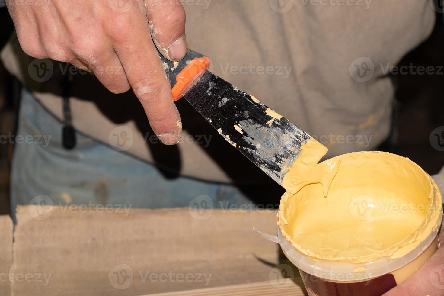 les mains ramassent le mastic avec une spatule de la boîte photo