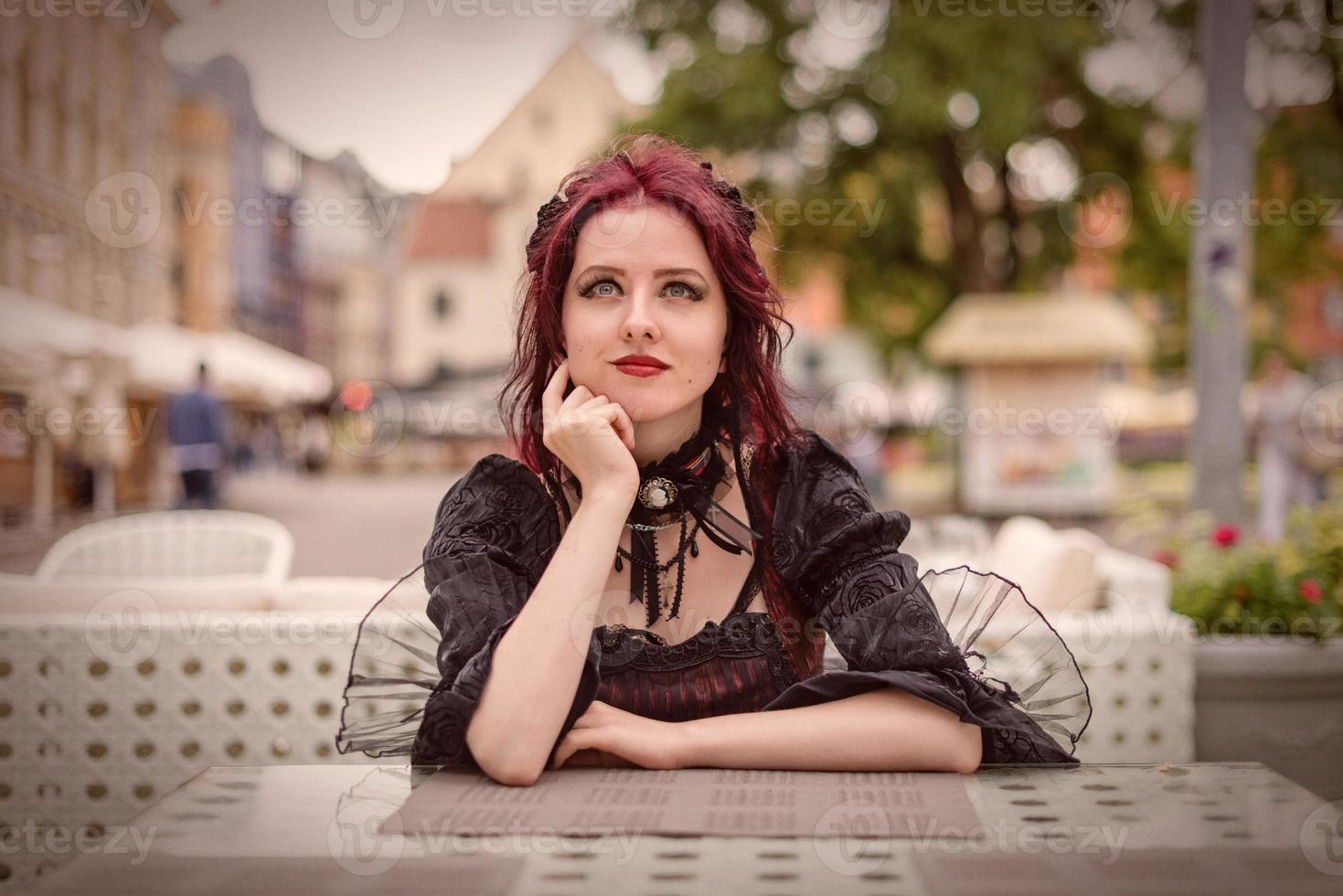 jeune femme rousse magnifique assise dans un café en plein air vêtue de vêtements de mode rétro. photo