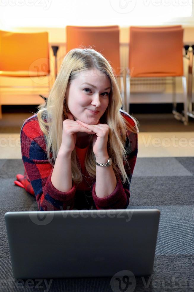 une femme blonde souriante dans une chemise à carreaux rouge allongée sur le sol devant l'ordinateur. photo