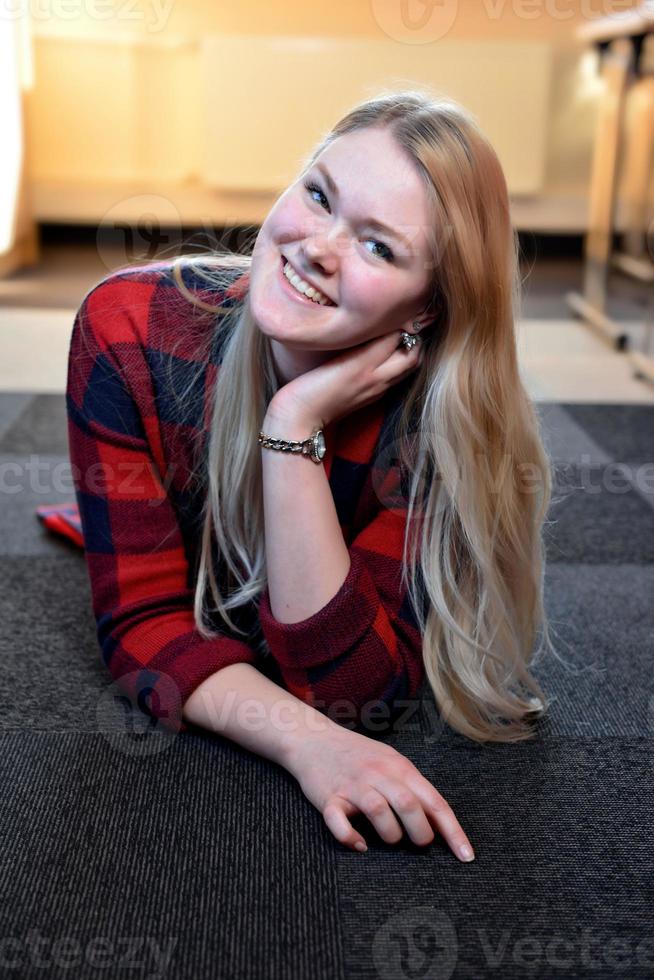 une femme blonde souriante dans une chemise à carreaux rouge allongée sur le sol. photo