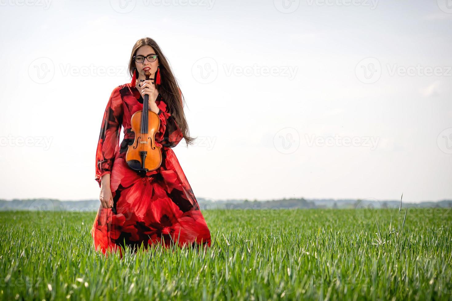 Jeune femme en robe rouge avec violon dans un pré vert - image photo