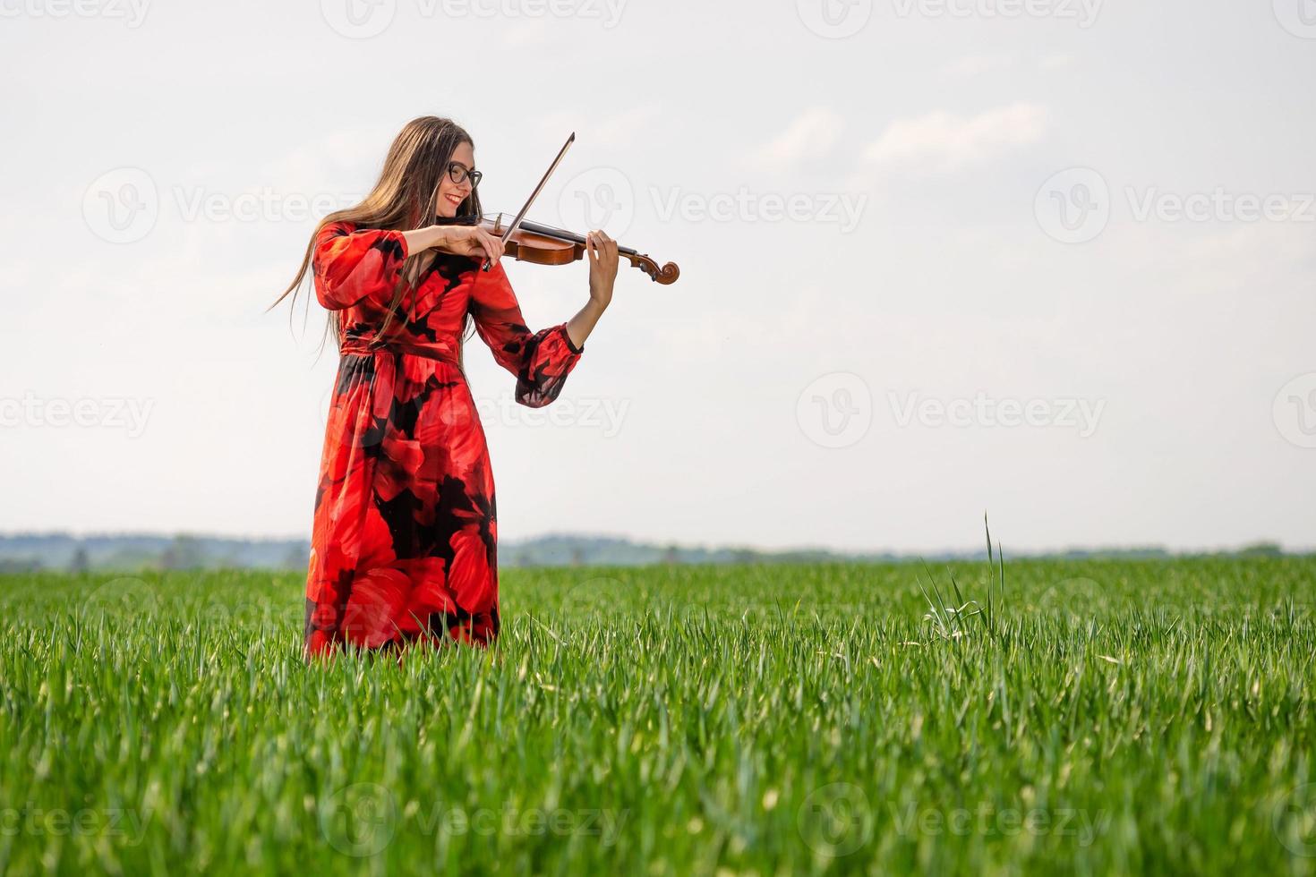 Jeune femme en robe rouge jouant du violon dans un pré vert - image photo