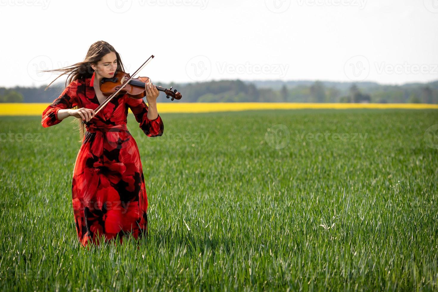 Jeune femme en robe rouge jouant du violon dans un pré vert - image photo