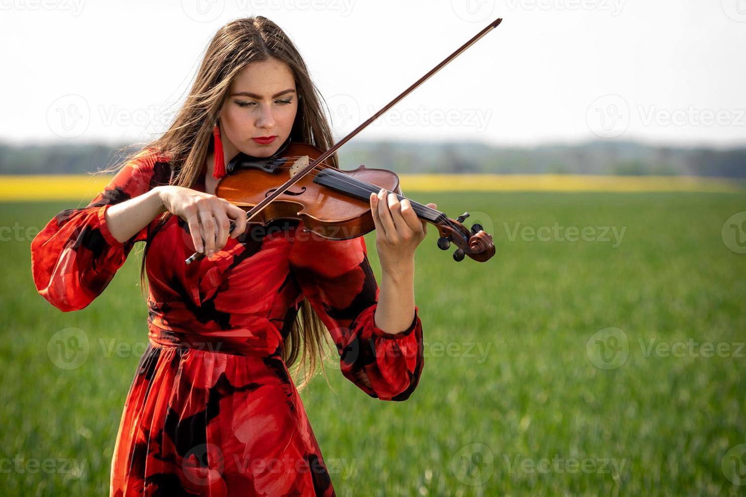 Jeune femme en robe rouge jouant du violon dans un pré vert - image photo