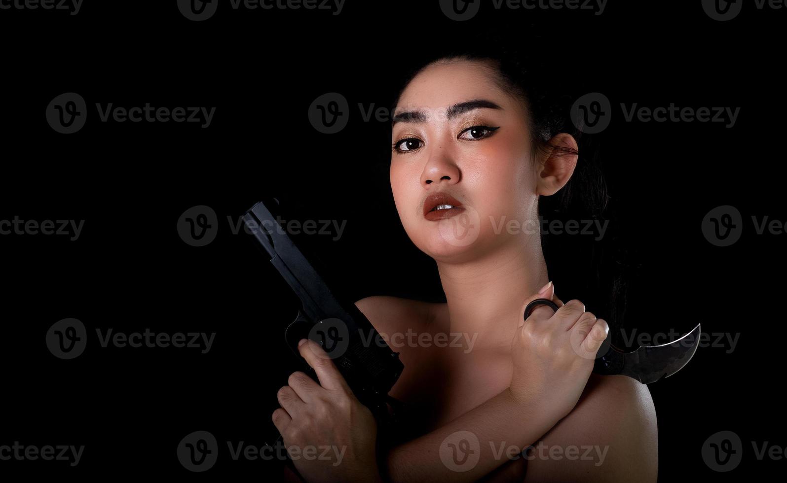 Asie femme une main tenant un pistolet et un couteau karambit sur fond noir photo