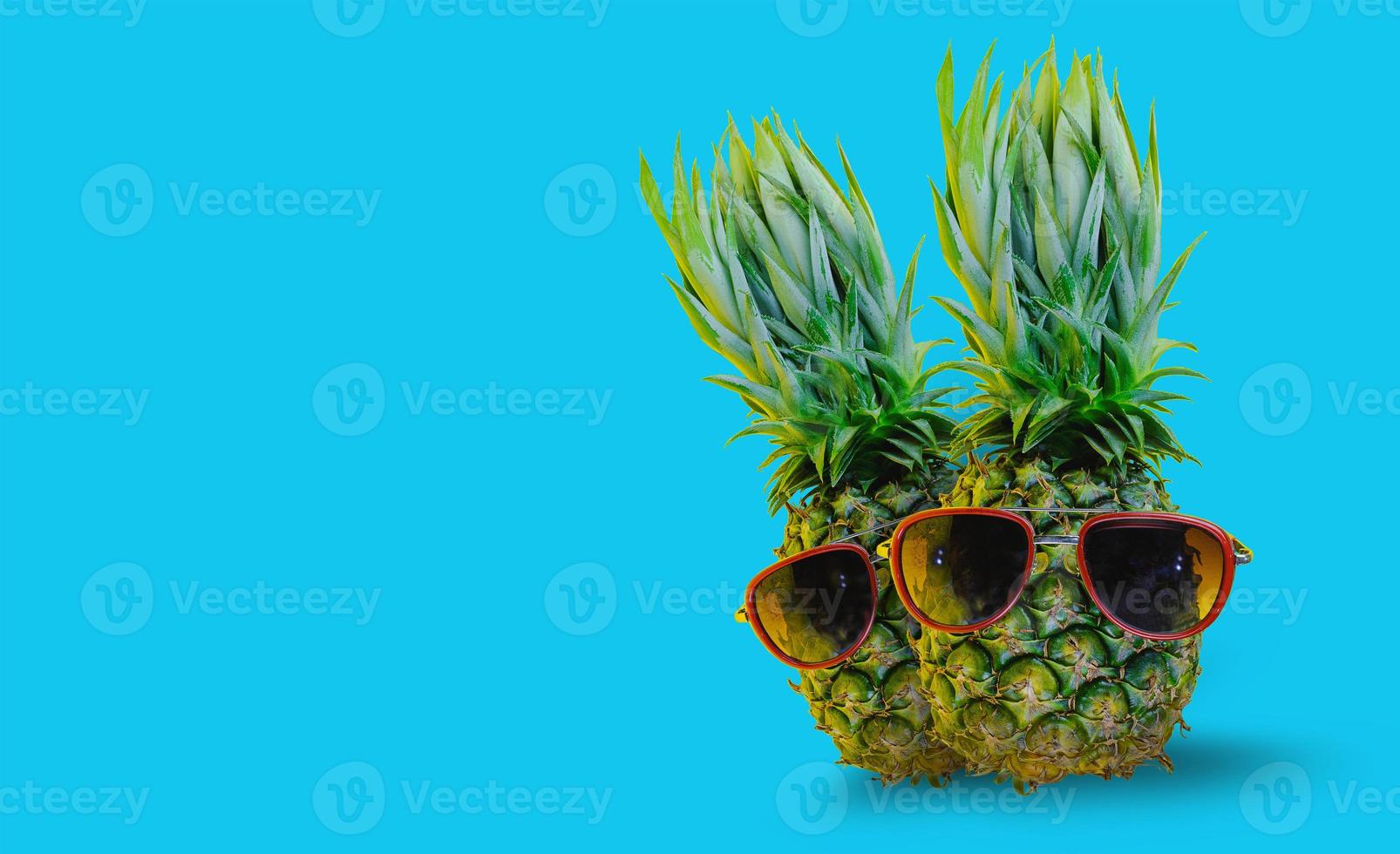 ananas portant des lunettes de soleil rouges sur fond bleu isolé photo