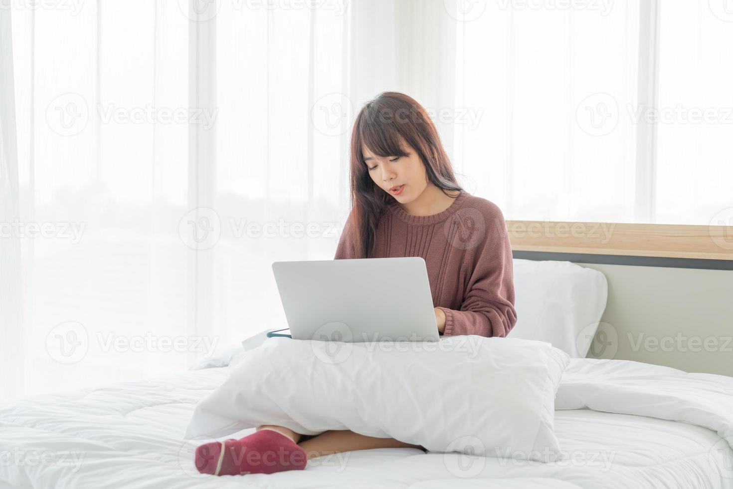 femme asiatique travaillant avec un ordinateur portable sur le lit à la maison photo