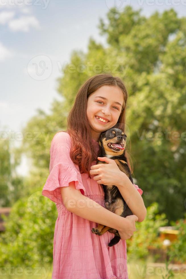 une adolescente avec un chien chihuahua dans ses bras sur un arrière-plan flou d'arbres sourit. photo