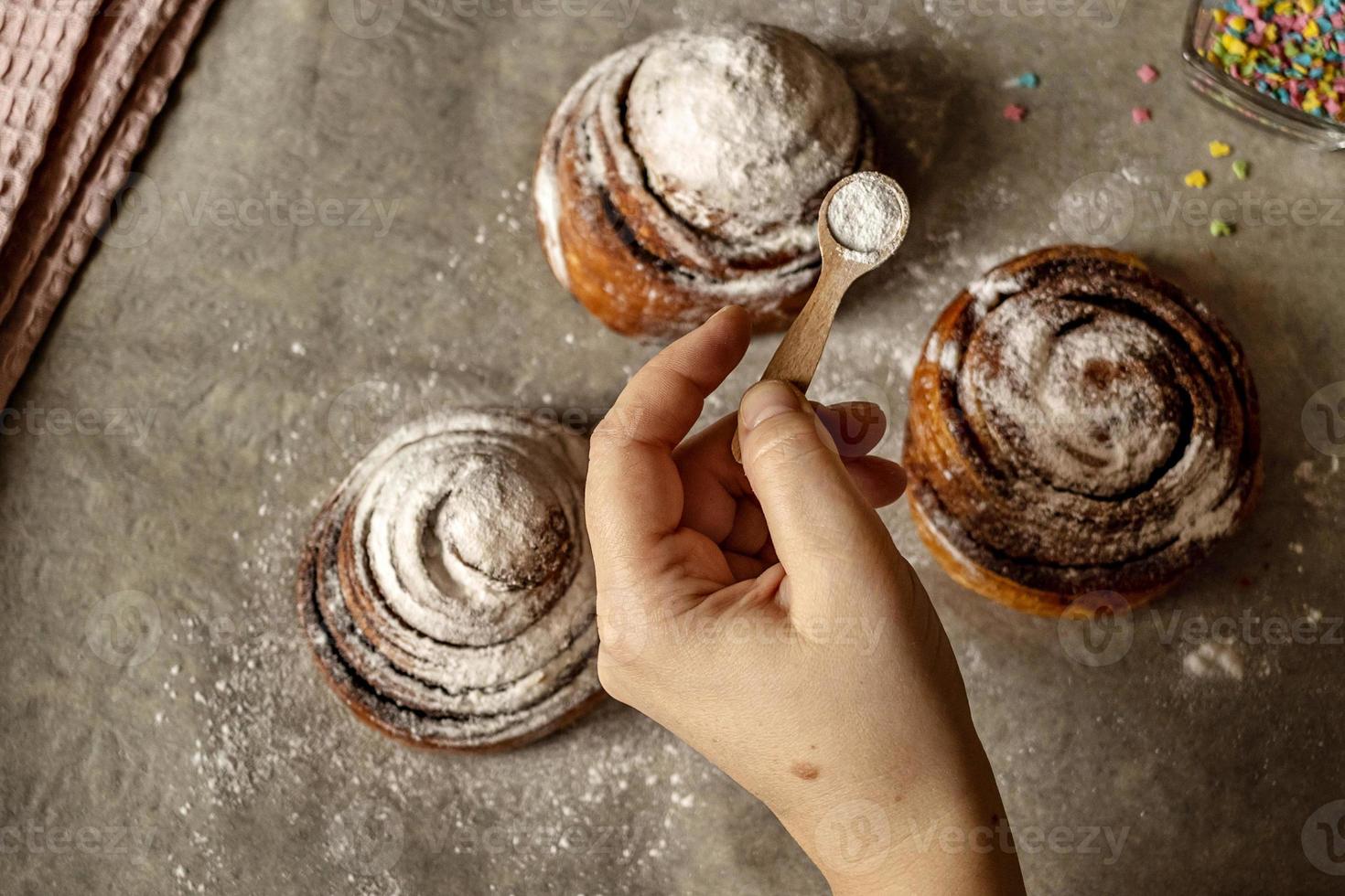 la main de la femme saupoudre de sucre glace sur des brioches à la cannelle fraîchement cuites photo