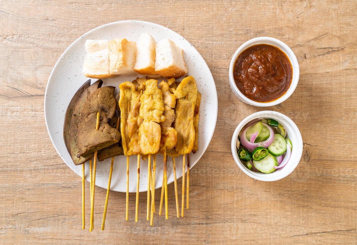 satay de porc et satay de foie avec du pain et de la sauce aux arachides et des cornichons qui sont des tranches de concombre et des oignons au vinaigre - style de cuisine asiatique photo