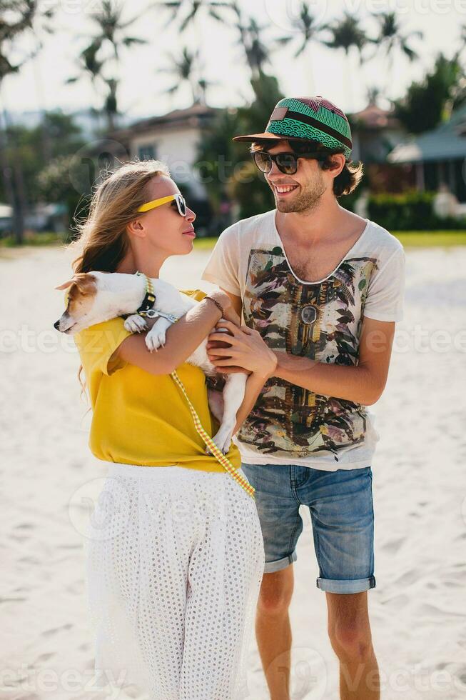 branché Jeune élégant branché couple dans l'amour en marchant en jouant chien chiot jack Russell dans tropical plage, blanc sable, cool tenue, romantique humeur, ayant amusant, ensoleillé, homme femme ensemble, vacances photo