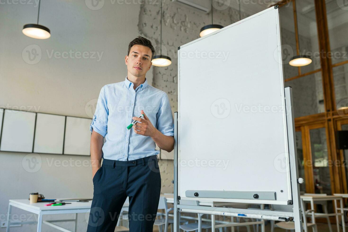 sur de soi Jeune Beau souriant homme permanent à vide blanc planche avec marqueur photo