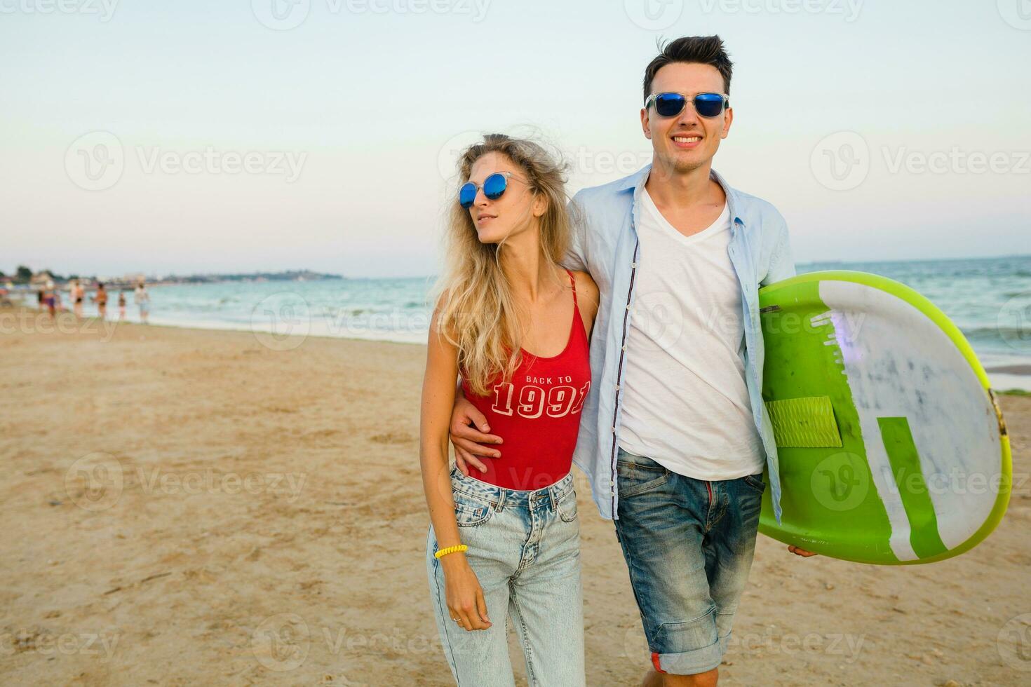 Jeune souriant couple ayant amusement sur plage en marchant avec le surf planche photo