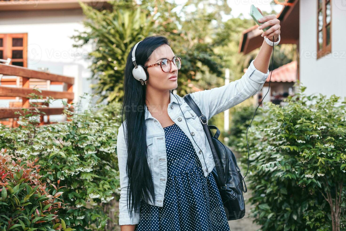 Jeune élégant femme en marchant avec téléphone intelligent, écoute à la musique sur écouteurs photo