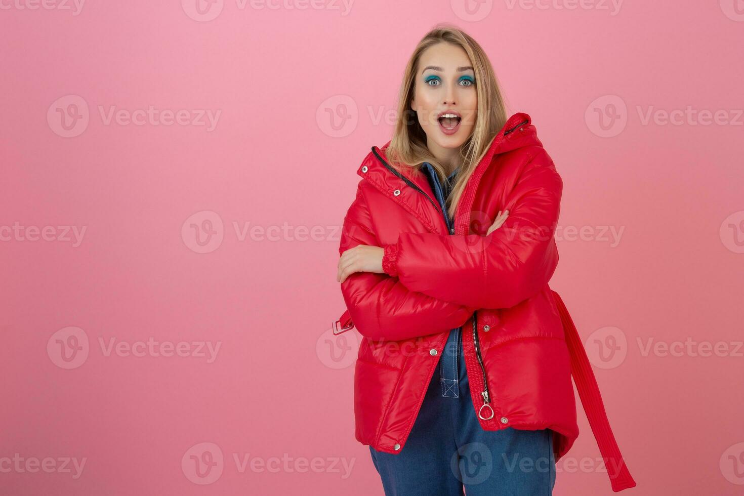 blond content attrayant actif femme posant sur rose Contexte dans coloré hiver vers le bas veste de rouge couleur, ayant amusant, chaud manteau mode s'orienter, souriant photo