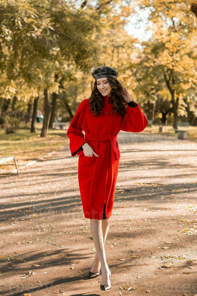 attrayant élégant femme en marchant dans parc habillé dans chaud rouge manteau photo