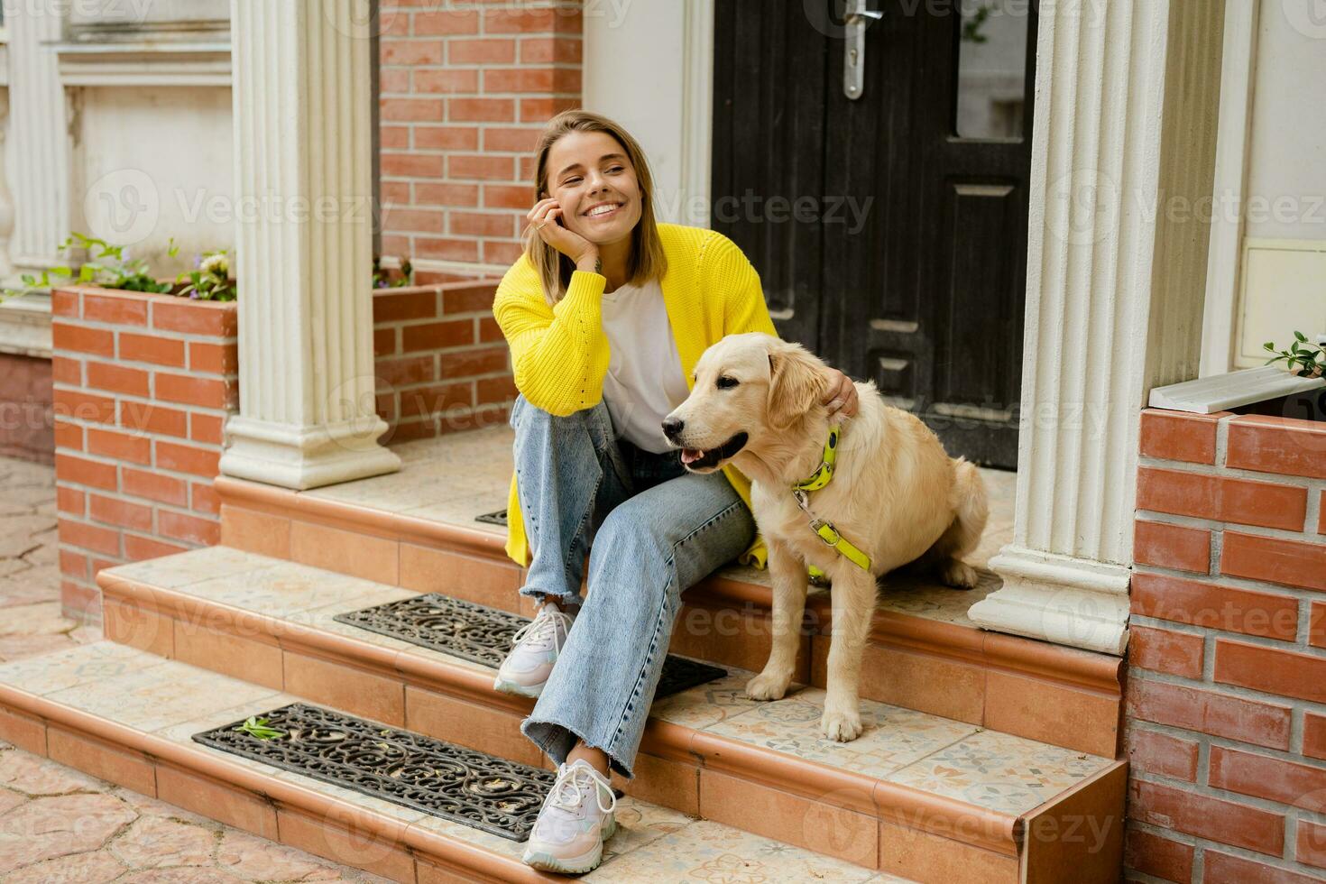 content souriant femme dans Jaune chandail en marchant à sa maison avec une chien d'or retriever photo