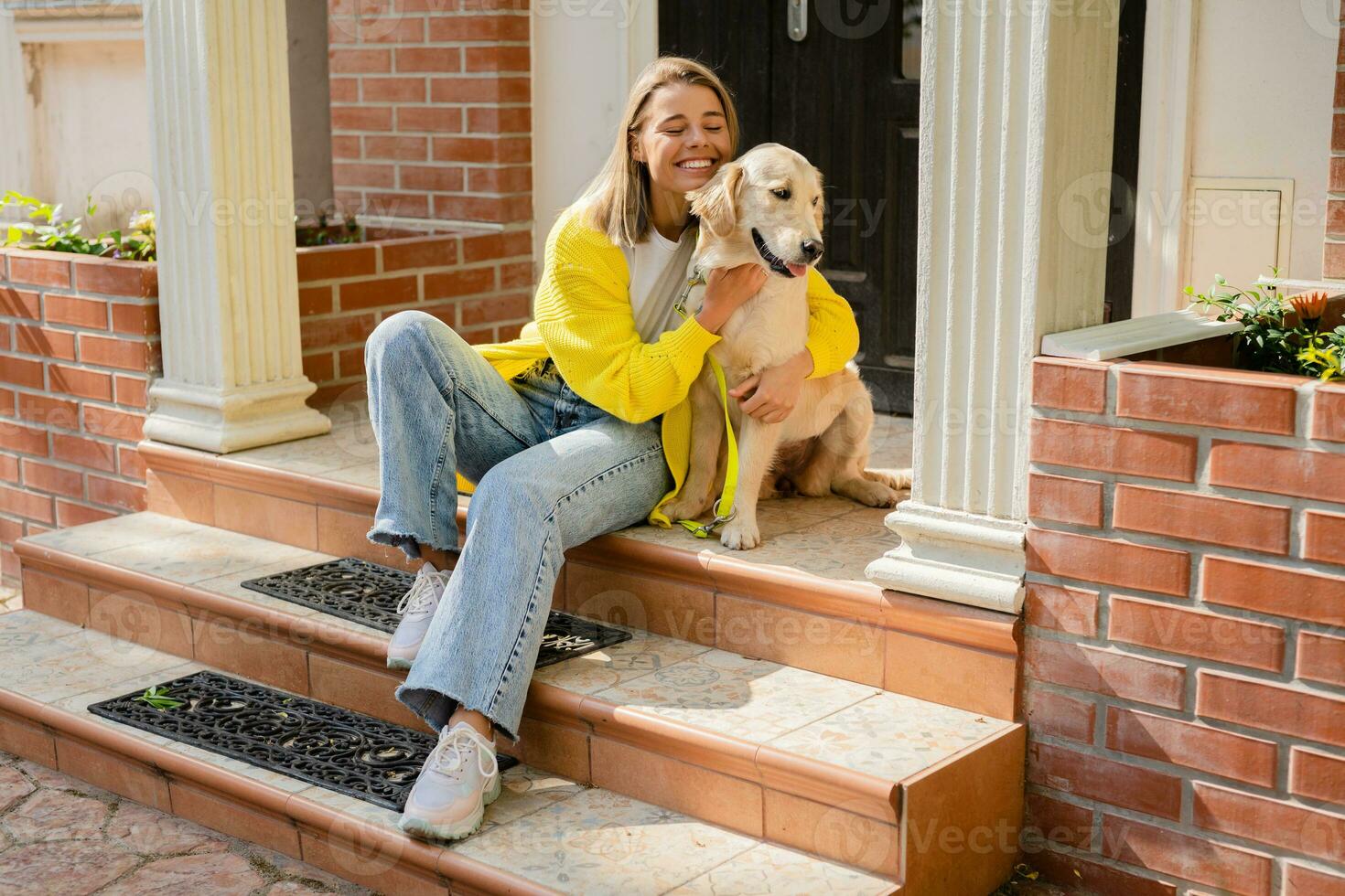 content souriant femme dans Jaune chandail en marchant à sa maison avec une chien d'or retriever photo